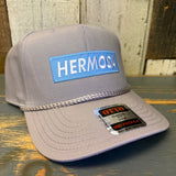 Gray cap with 'HERMOSA' logo on a wooden surface
