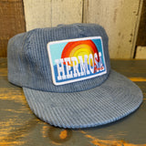Slate blue corduroy cap with a colorful patch on a wooden surface