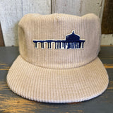 Beige corduroy hat with a blue Manhattan pier embroidered design on a wooden surface.