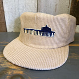 Beige corduroy cap with blue and white logo on a wooden surface