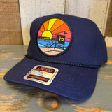 Navy blue cap with a colorful patch featuring a beach scene on a wooden surface.