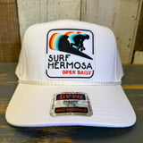 White cap with 'Surf Hermosa' logo on a wooden surface