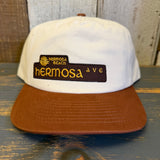 White and brown cap with 'Hermosa Beach Hermosa Ave' logo on a wooden surface.