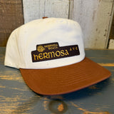 White and brown cap with 'Hermosa Beach Hermosa Ave' logo on a wooden surface.