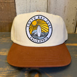 White cap with brown bill featuring a 'South Bay Surf California' logo on a wooden surface.
