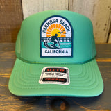 Cactus green trucker hat with surfer, sun, and pier patch; mesh back; adjustable snap closure for casual wear.
