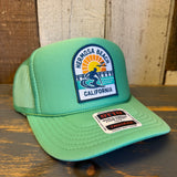 Cactus green trucker hat with surfer patch, adjustable snapback, mesh back, suitable for casual outdoor wear.