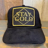 Black cap with 'Stay Gold' embroidery on a wooden surface.