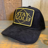 Black cap with 'Stay Gold' embroidery on a wooden surface.