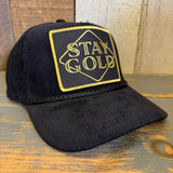 Black cap with 'Stay Gold' embroidery on a wooden surface.