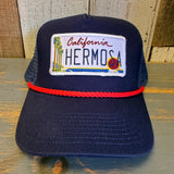 navy blue mesh and cloth trucker hat with a California Hermosa license plate patch on a wooden surface