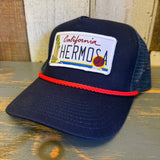navy blue mesh and cloth trucker hat with a California Hermosa license plate patch on a wooden surface
