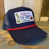navy blue mesh and cloth trucker hat with a California Hermosa license plate patch on a wooden surface
