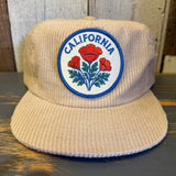 Beige corduroy cap with California poppy emblem on a wooden surface