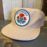 Beige corduroy cap with California poppy emblem on a wooden surface