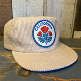Beige corduroy cap with California poppy emblem on a wooden surface