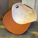 back of a white canvas trucker hat with a black and white 'South Bay Surf California' patch and a mustard brown brim on a wooden surface