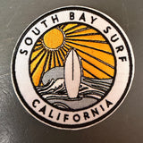 Round embroidered patch featuring a surfboard, sun rays, and waves. Ideal for accessorizing bags or jackets.