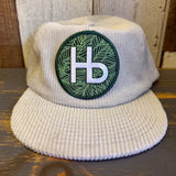white corduroy cap with a green and white HB patch on a wooden surface