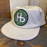 white corduroy cap with a green and white HB patch on a wooden surface