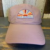 dusty rose baseball cap with colorful Muy Hermosa logo on a wooden surface