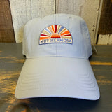 Light blue grey cap with colorful sunset design and Muy Hermosa text on a wooden surface.