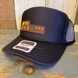 A black high crown trucker hat with mesh panels sits on a wooden surface, designed for casual beachwear.
