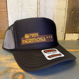 Black-and-white high crown trucker hat with mesh panels rests on a wooden surface, suitable for casual wear.