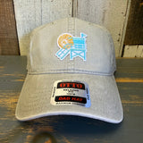 Stone cotton dad hat, 6-panel low profile, lifeguard tower and sun design, displayed on wood alongside stickers.