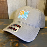 Stone cotton dad hat with lifeguard tower patch and stickered brim, displayed on a wooden surface.