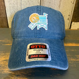 Sky blue cotton dad hat with colorful Lifeguard Tower 6 patch and OTTO sticker, ideal for casual beachwear.
