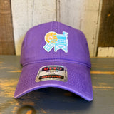 Purple cotton dad hat with lifeguard tower design displayed on a wooden surface against a rustic background.