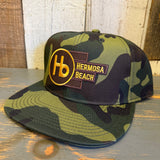 Camo 6-panel cotton hat with adjustable strap resting on a wooden surface, suitable for casual outdoor wear.