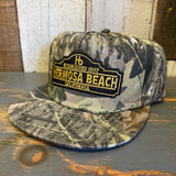 Green camo 5-panel surf hat with embroidered Hermosa Beach text; lightweight cotton for casual outdoor wear.