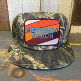 5-panel camouflage surf hat displayed on a rustic wooden surface, suitable for casual or outdoor wear.