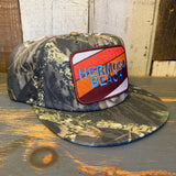 Camo-patterned 5-panel hat with patch, made from fabric, displayed on a wooden surface.