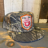 Surf camo 5-panel hat with Smokey Bear patch made of fabric, displayed on a wooden surface, suitable for casual wear.