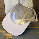 Faded bone 6-panel trucker hat, retro sunset design, made of fabric and mesh, lies upside down on a wooden surface.