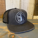 Faded black 6-panel trucker hat with mesh panels sits on a rustic wooden surface, highlighting its casual style.