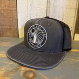 Faded black 6-panel trucker hat with mesh back, displayed on a wooden surface. Suitable for casual or outdoor wear.