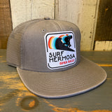 Faded grey 6-panel mesh trucker hat with a surfer patch and rainbow wave design.