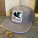 Faded grey 6-panel trucker hat with mesh back, featuring a patch and rainbow stripes. Casual and breathable for everyday use.