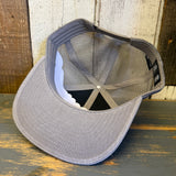 Faded grey 6-panel trucker hat displayed upside down on a wood surface, mesh and fabric visible.