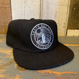 Black 6-panel strapback surf hat made of fabric, displayed on a wooden surface.