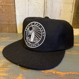 Black 6-panel strapback hat made of fabric, displayed on a wooden surface, suitable for casual or outdoor use.