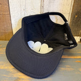 An upside-down, black 6-panel cotton strapback hat rests on weathered wood.