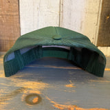 Forest green foam trucker cap, mesh back, displayed from behind on rustic wooden surface.