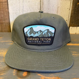 Cypress green 5-panel hat with Grand Teton National Park 1929 text, displayed on a wooden surface.