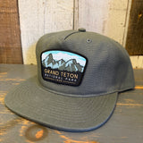 Cypress green 5-panel hat with Grand Teton National Park 1929 text, shown on a wooden surface.