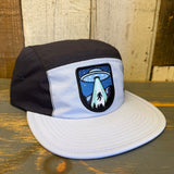 Black and grey two-tone nylon cap with UFO Bigfoot graphic sits on a wooden surface.